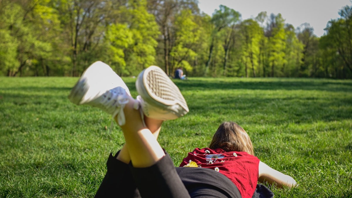 woman in black pants and red shirt lying on green grass field during daytime